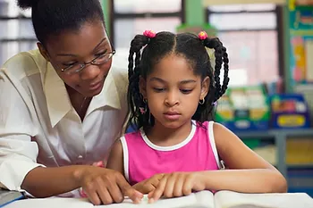 A teacher reading aloud to a young female student.