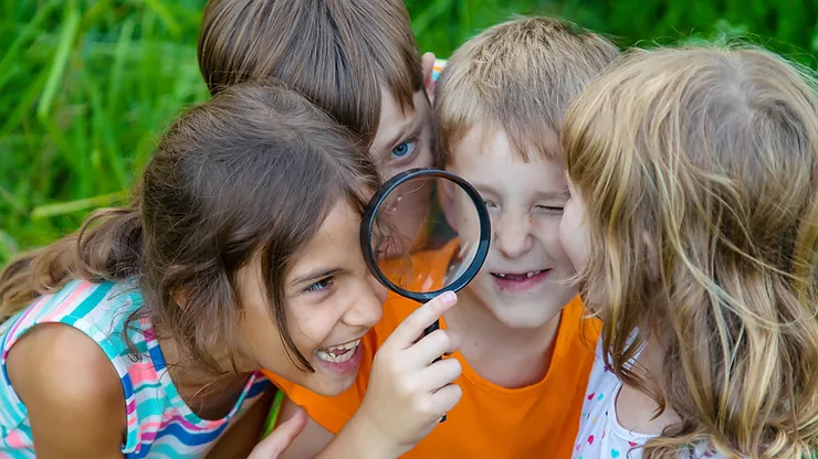Kids with magnifying glass outdoors exploring.
