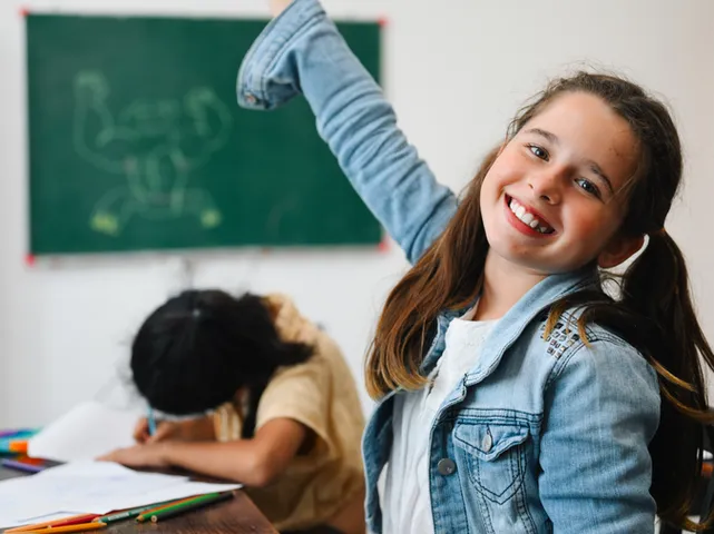 A smiling girl raising her hand in class